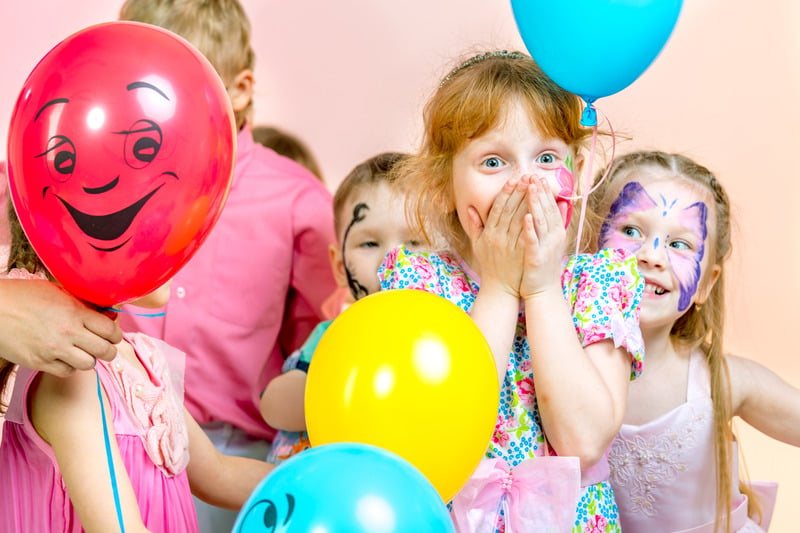 Crianças com balões coloridos e o rosto pintado durante a festa